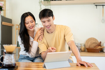 Obraz premium Asian man and woman couple watching video on tablet as making drip coffee at kitchen cooking counter