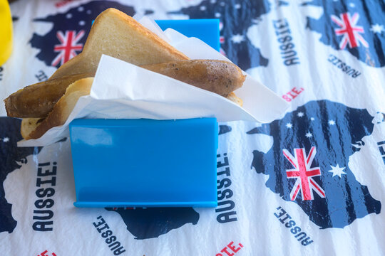 A classic Australian sausage sizzle served on white bread in a blue holder, featuring a patriotic Aussie-themed tablecloth. Perfect for community BBQ events and Australian culture promotions.