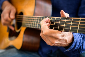 Musician's hands playing acoustic guitar with focus on fretboard chord position and strumming technique. Ideal for music lesson platforms, guitar instruction materials, and creative hobby marketers.