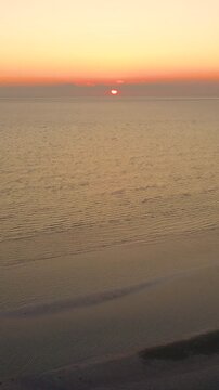 Vertical drone sunset over Cape Cod shoreline, warm glow reflecting on shallow pools and low tide sandbars. Tall-frame seascape with gentle surf, cinematic b-roll.