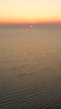Vertical drone sunrise over Cape Cod beach at low tide, sun glow reflecting through braided channels and sandbars. Vertical coastal morning scene with gentle waves.