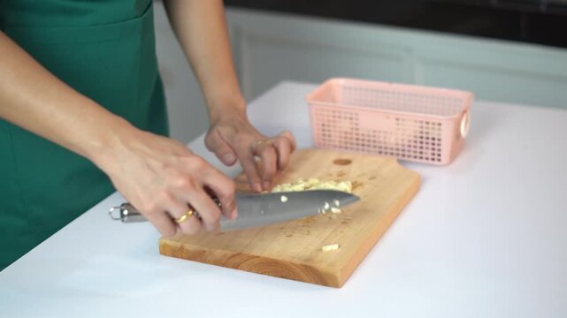 Professional chef hands finely mincing garlic on a wooden board for cooking seasoning