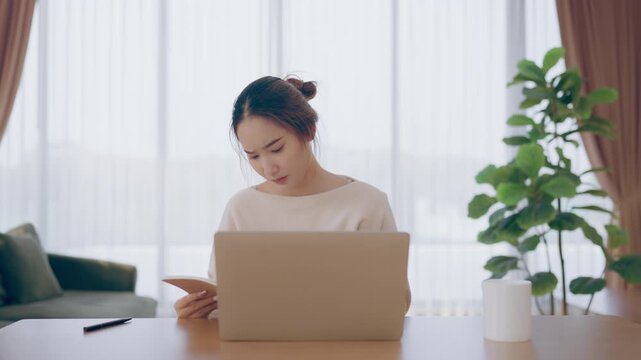 Young Asian woman working in living room, she has a headache due to long and overworking leaving her tired and dizzy. Concept of sickness from work and office syndrome