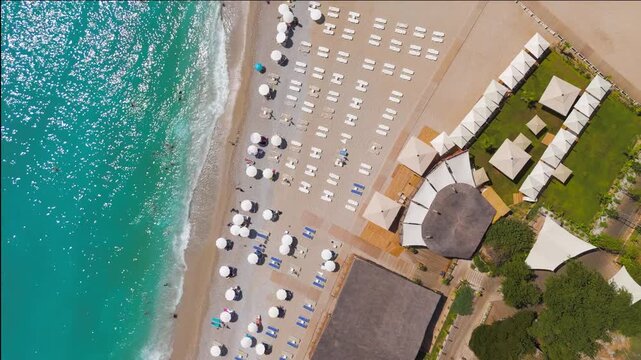 Oludeniz, Turkey. Aerial top down view of crowded Oludeniz Beach with rows of colorful umbrellas, many vacationers on pebble shore, sea waves crashing, summer. Aerial View, HEAD OVER SHOT, HEAD OVER 