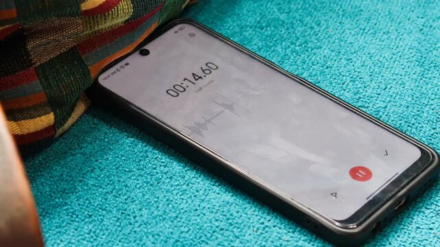 Voice detection and recording app in mobile phone listening to contestation laying on couch or sofa hidden from view. Secretly grabbing and wiretapping inside home or apartment during covert operation