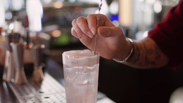 Serving drink. Ice cream soda. Bartender hand adding blooming lavender sprig to cold water in glass. Refreshing cocktail with whipped white top.