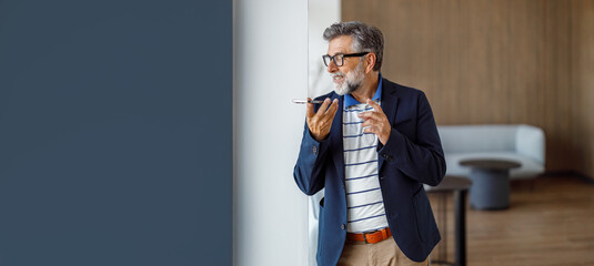Male professional in eyeglasses standing in corporate office discussing ideas while speaking over...