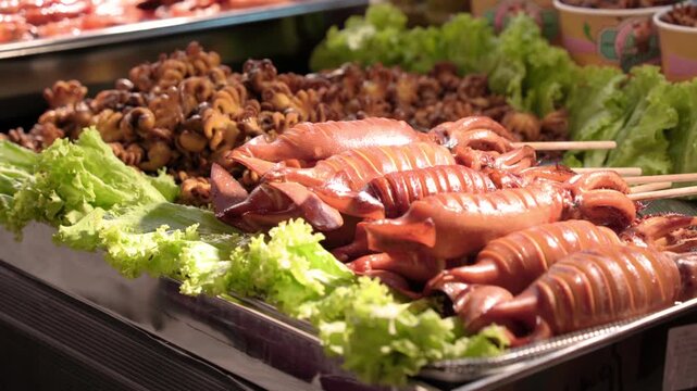 Fresh raw squid skewers displayed on a stainless steel tray at a seafood market or street food stall.