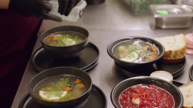 Preparing food. Kitchen process. Chef garnishing hot dish with chopped fresh herbs. Hands adding greens in soup borsch ring desk bell.