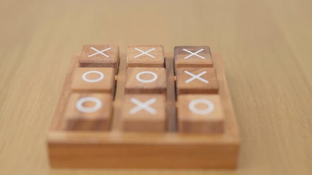 Hand holding and playing wooden block of tic tac toe game. A completed game of noughts and crosses or Xs and Os game. Challenge, Competition, winning, tactic, strategy and recreation concepts