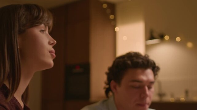 Medium close up shot of young Caucasian boyfriend and girlfriend eating snacks while having romantic dinner at home in warm light