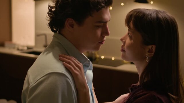Medium close up shot of loving Caucasian young partners looking at each other while dancing in cozy home kitchen