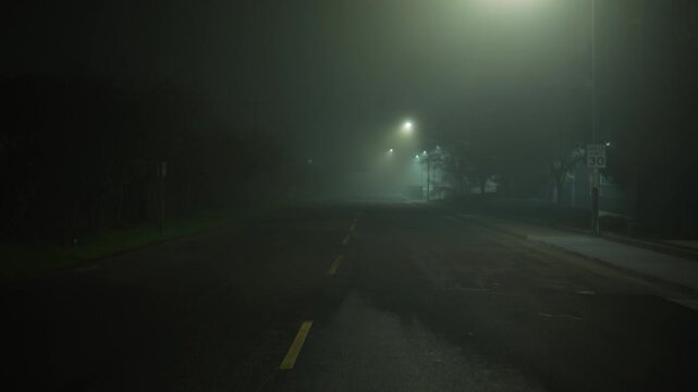 Slow forward camera movement along empty foggy street, cinematic night road with diffused streetlight glow and growing sense of isolation
