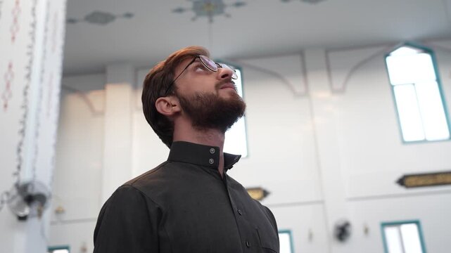 Young Muslim man in traditional thobe looking at Islamic architecture and mosque decorations. Ramadan spiritual reflection and appreciation of masjid design. Islamic culture and heritage concept.