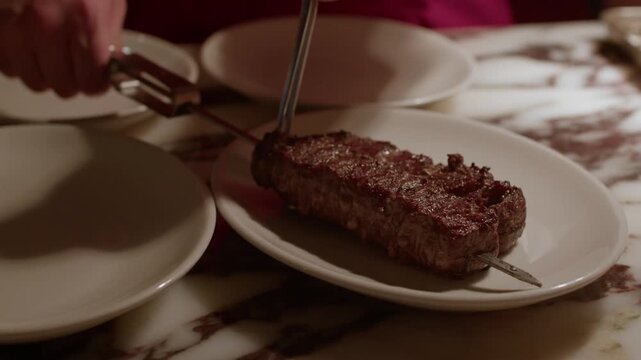 A detailed close-up shot of a chef using professional metal tongs to carefully plate a juicy, perfectly grilled meat skewer on a clean white dish in a gourmet kitchen