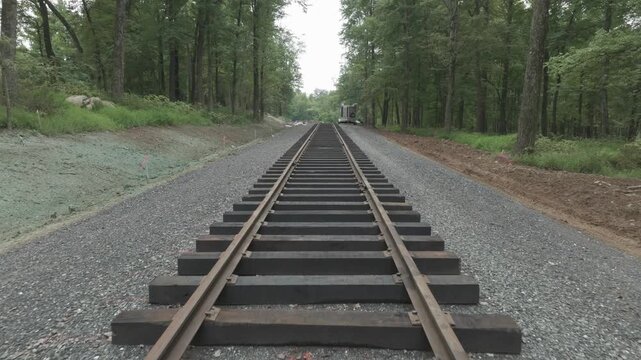 View of train tracks running through a forested area. The path shows different conditions and updates along the track. The environment has trees and gravel surroundings.