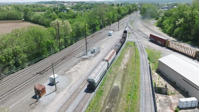 A vintage steam freight train makes its way backing up in yard performing switching operations moving steadily along the railway tracks in a peaceful countryside setting.