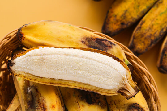 Closeup of a basket filled with ripe yellow saba bananas (pisang kepok). With one fruit peeled to show its center. Captured with natural light on a yellow background.