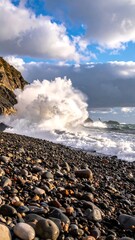 A wave crashes on a pebble beach under a dramatic sky
