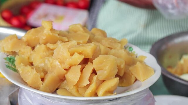 Traditional Indonesian steamed cassava snack on white plate in outdoor market with natural light