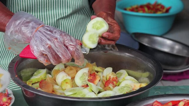 Street food vendor peeling fresh cucumber for traditional Indonesian rujak salad with natural light