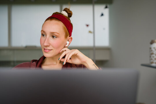 Woman working remotely with laptop and earbud in modern home office