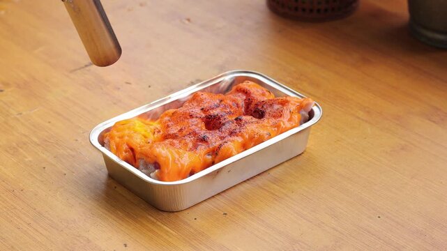 Indonesian dimsum mentai being seared with kitchen torch on wooden table with natural light