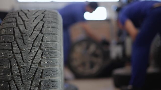 Mechanic installing car winter tires in garage workshop with focus on tread details.
