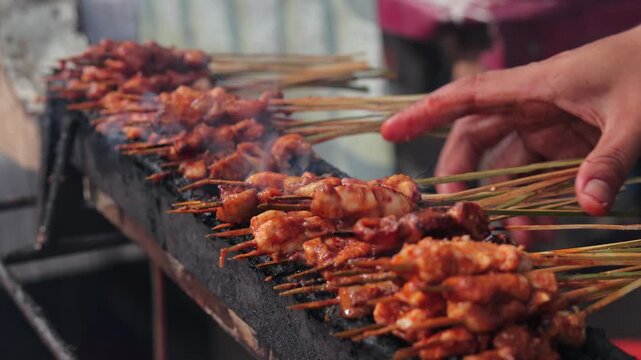Traditional Indonesian chicken satay grilling on charcoal stove with natural light at street food market