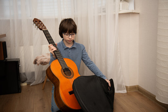 Young musician holding a classical acoustic guitar and gig bag in a cozy home interior.