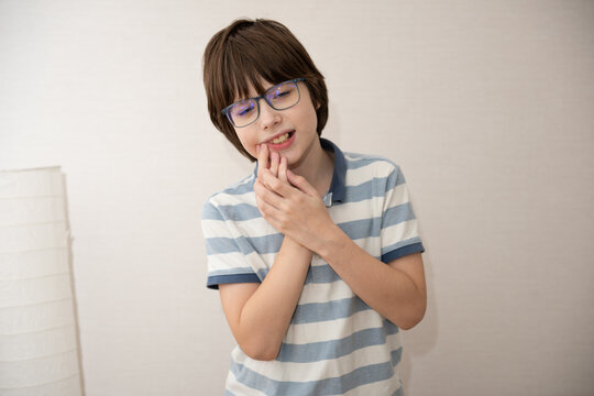 Sad little Asian boy suffering from toothache pain in mouth while eating candy, holding his cheek, dental pain.