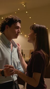 Vertical medium shot of tender Caucasian couple slow dancing in cozy living room under warm lighting