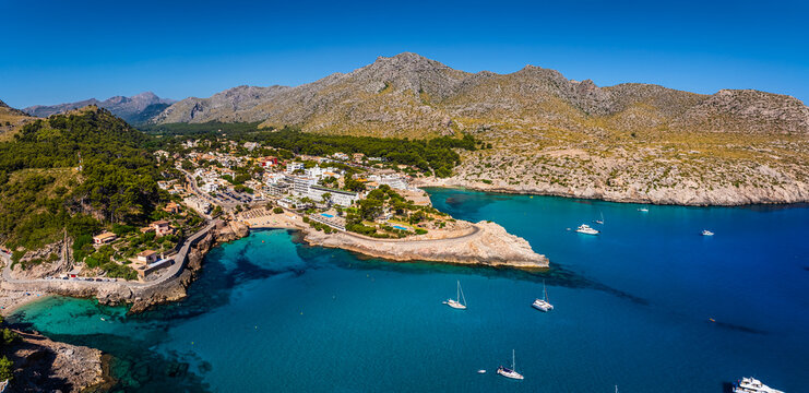 Mallorca, Spain - Aerial Panoramic view of Cala Sant Vicenc on the island of Mallorca at daytime with Cala Clara and Cala Molins bays, beach, hotels, yachts and mountains at background with blue sky