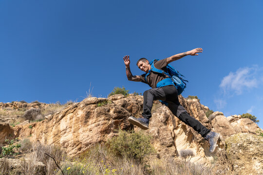 Male hiker backpacker jumping over rocky terrain