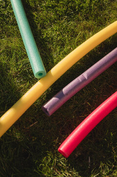 Colorful pool noodles laying on green summer grass in backyard