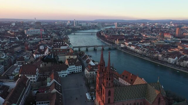 Basel, Switzerland: Cinematic aerial drone footage of the Basel cathedral, the Basler Munster, along the Rhine river that flow through the medieval old town at sunset in Switzerland