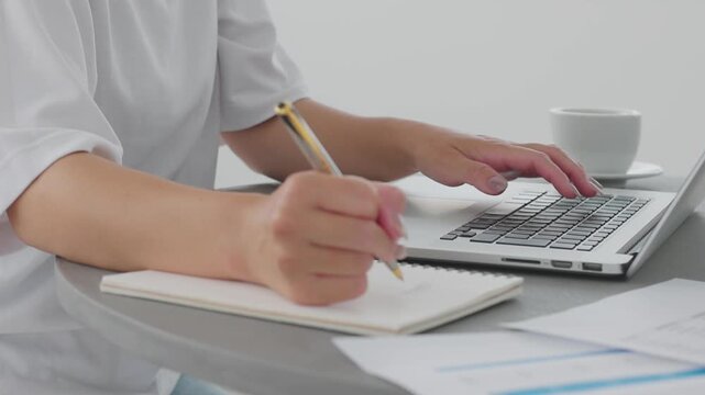 Close-up of woman's hands working on laptop and taking notes