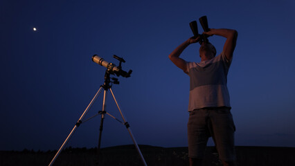 Fototapeta premium Amateur astronomer using telescope and binoculars for watching stars, Moon, planets and other celestial objects from a field in nature.