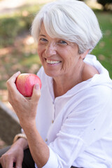 healthy looking senior woman with grey hair eating apple