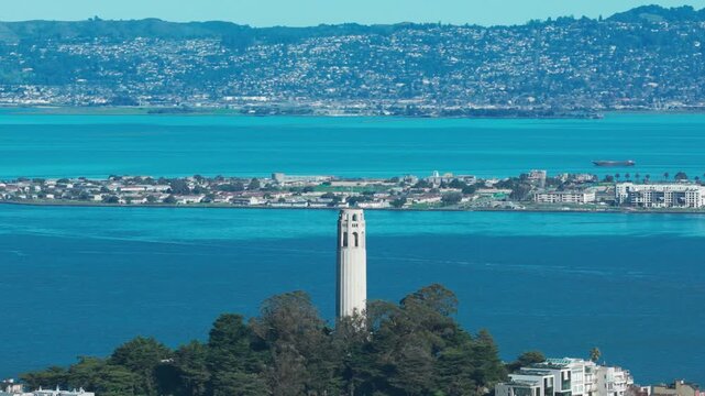 Aerial telephoto panning shot of Coit Tower with Treasure Island in the distance on a bright sunny day in San Francisco. 4K