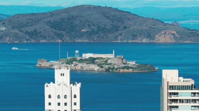 Telephoto dolly aerial shot of Alcatraz Island framed by skyscrapers on a perfect day in San Francisco, California. 4K