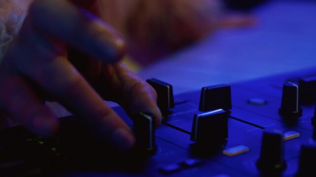 Man DJ playing music on electronic mixer controller at disco club. Male disk jockey mixing sound on set in night club. Hand of guy on turntable panel. Close up. Clubbing vibe, neon party, mix console