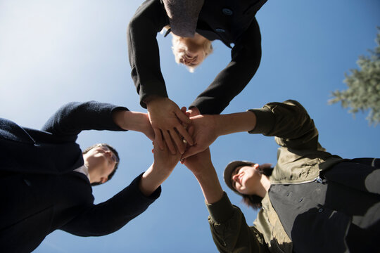 Worm's eye view of three women stacking their hands under blue sky