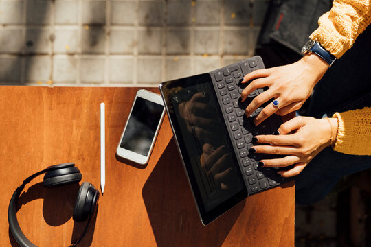 Hands of female student typing on digital tablet keyboard while sitting at sidewalk cafe in city