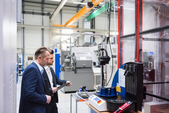 Two businessmen in factory shop floor examining machine