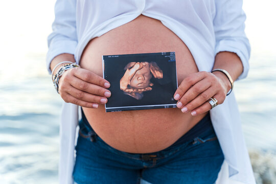 Midsection of pregnant woman showing sonogram while standing in font of water