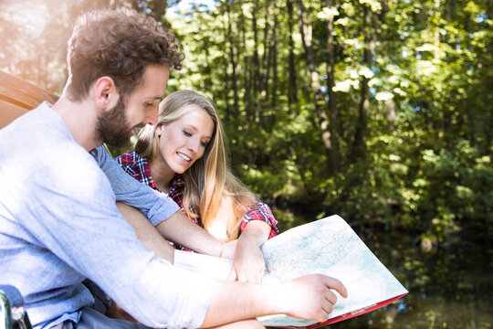 Smiling young couple reading map at a brook