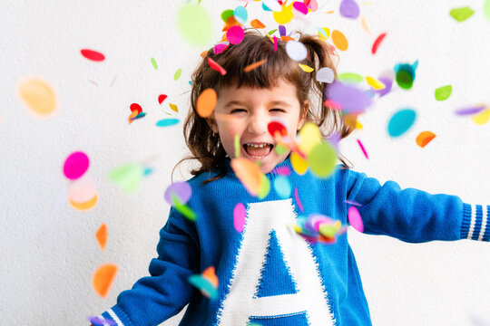 Happy little girl blowing the confetti at a party in front of a white wall