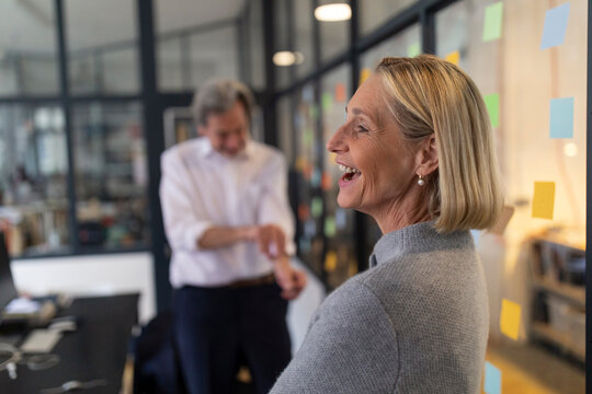 Happy businesswoman with colleague and sticky notes at glass pane in office