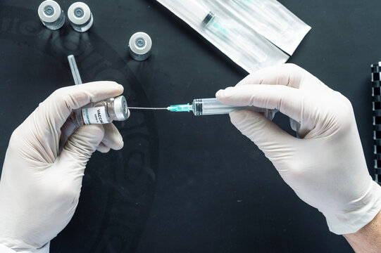 Cropped image of doctor's hand injecting syringe in vaccination vial over laptop at laboratory desk